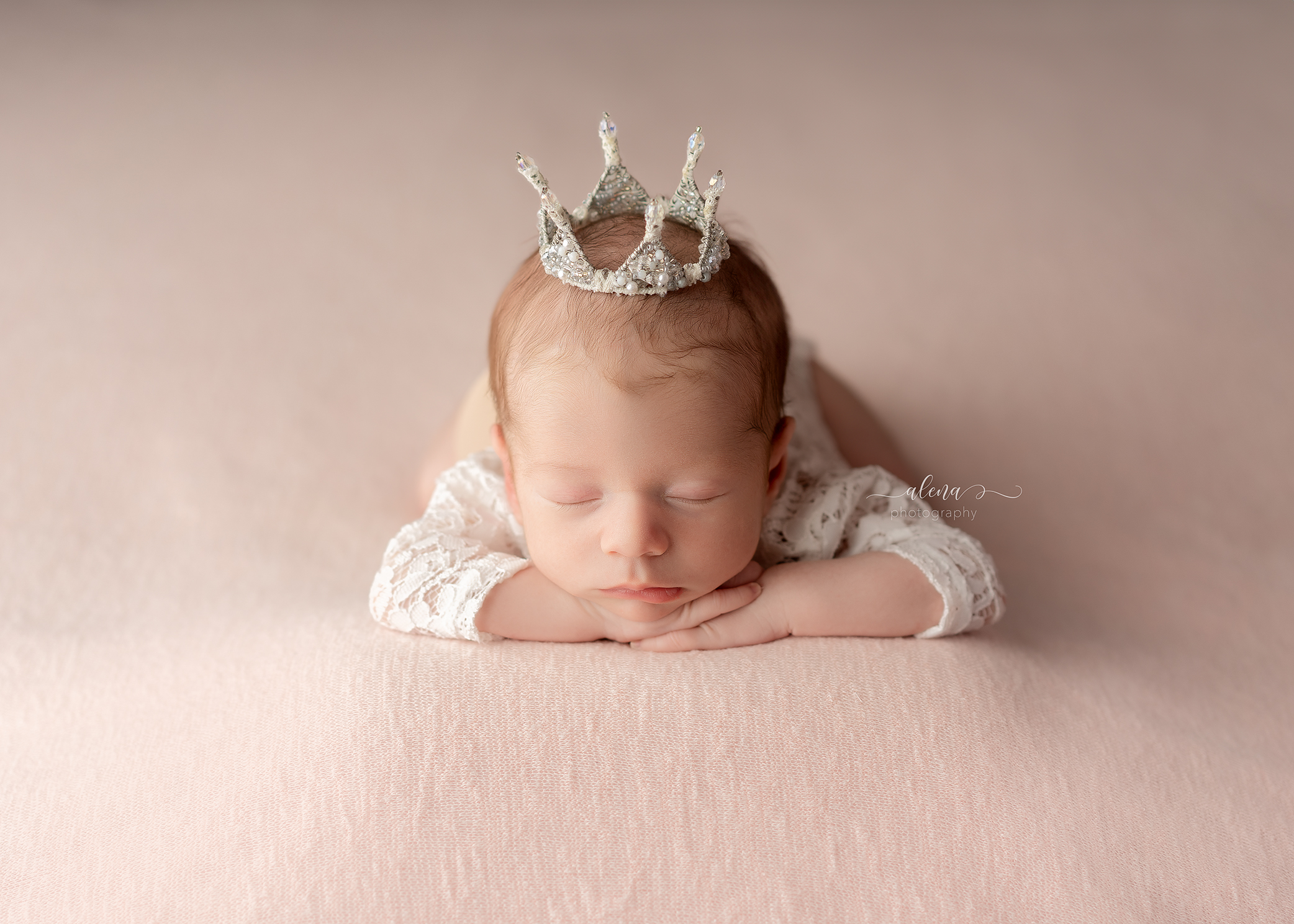 newborn baby girl with white crown in white outfit sleeping on pink blanket