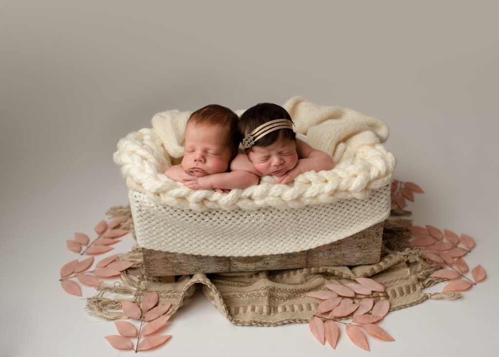Twin newborns posed together in wooden bowl with matching neutral tone