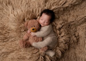 Newborn baby peacefully sleeping beside a soft teddy bear in a timeless portrait.