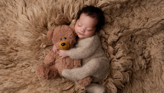 Newborn baby peacefully sleeping beside a soft teddy bear in a timeless portrait.