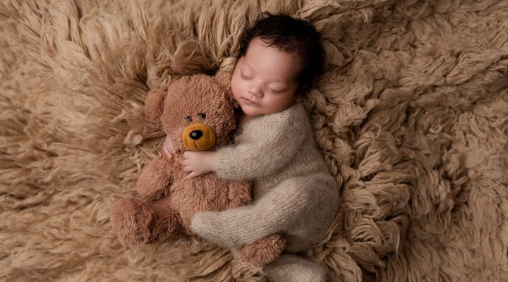 Newborn baby peacefully sleeping beside a soft teddy bear in a timeless portrait.