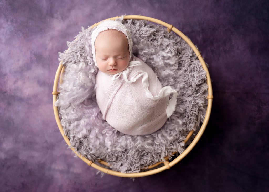 Wrapped newborn baby sleeping peacefully in a cream bowl with neutral blankets in a Charleston newborn photography studio.