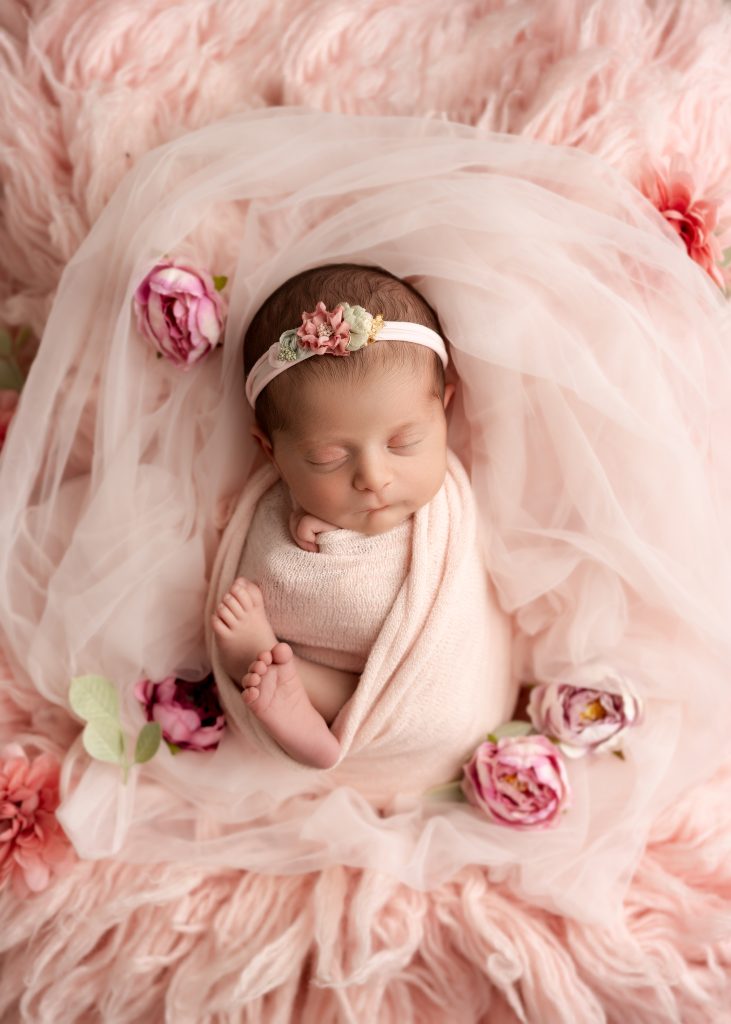 Wrapped newborn baby sleeping peacefully in a cream bowl with neutral blankets in a Charleston newborn photography studio.