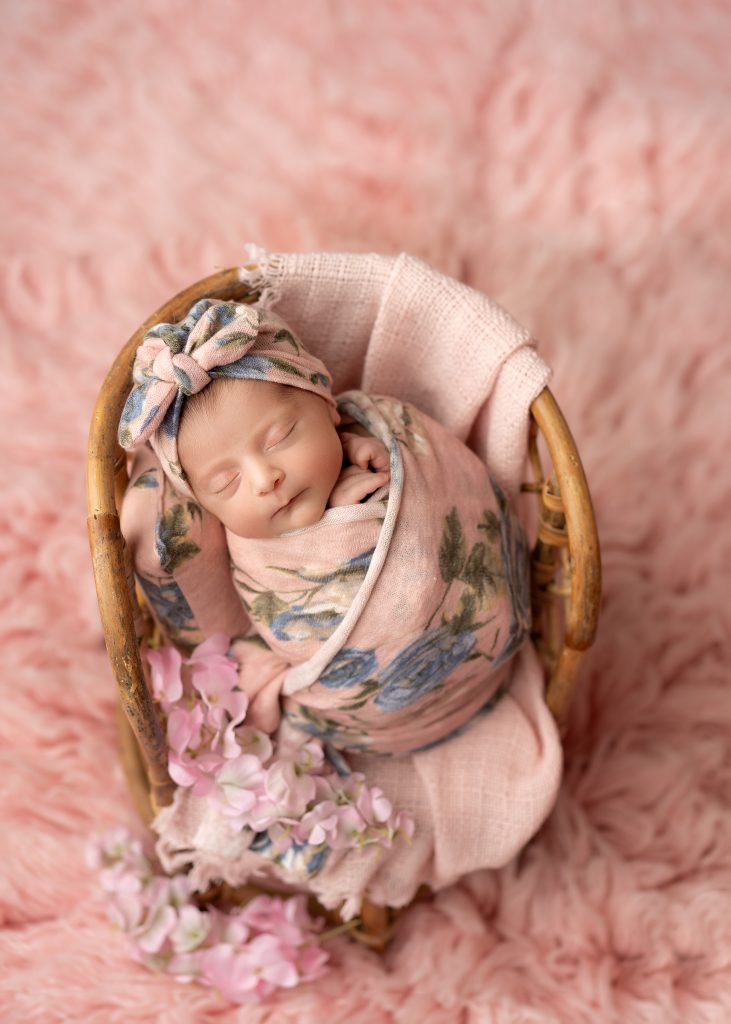 Wrapped newborn baby sleeping peacefully in a cream bowl with neutral blankets in a Charleston newborn photography studio.